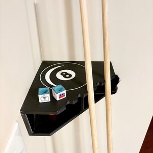 May include: Black wall-mounted pool cue rack with two cues, a brush, and two chalk holders. The rack has a white 8-ball design and the words "Valley View Billiard Club" on the chalk holder.