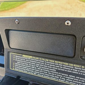 May include: A black textured dashboard panel featuring a silver ignition key switch labeled OFF and ON, and a rectangular warning label with yellow text detailing safety instructions, including a maximum vehicle payload of 800 lbs.