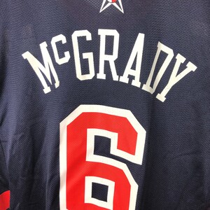 May include: A navy blue basketball jersey with the name "McGrady" and the number "6" in white and red lettering. A white star with a basketball inside is at the top of the jersey.