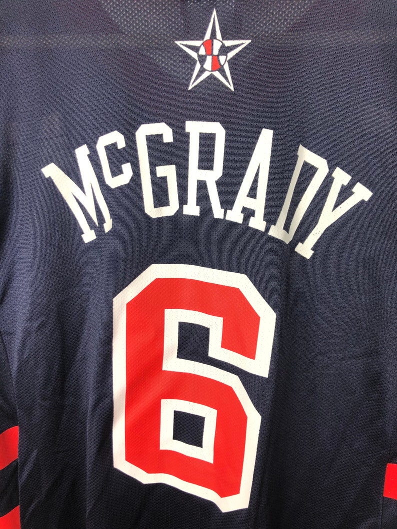 May include: A navy blue basketball jersey with the name "McGrady" and the number "6" in white and red lettering. A white star with a basketball inside is at the top of the jersey.
