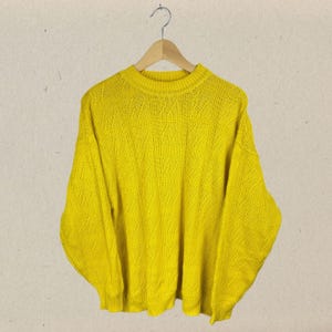May include: A bright yellow knitted sweater with a diamond pattern. The sweater has long sleeves and a crew neck.