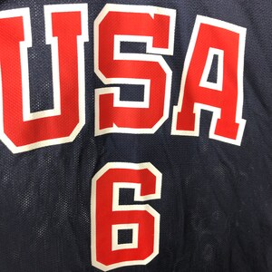 May include: A navy blue basketball jersey with the word "USA" in red with white outlines and the number "6" in red with white outlines.