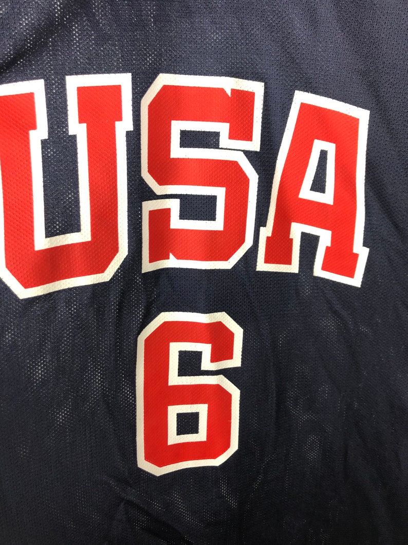 May include: A navy blue basketball jersey with the word "USA" in red with white outlines and the number "6" in red with white outlines.