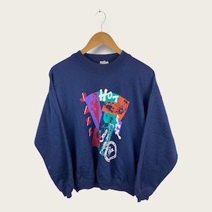 May include: A navy blue sweatshirt featuring a colourful graphic print of a person playing a saxophone with the text "Hot Jazz Hits" on the front.