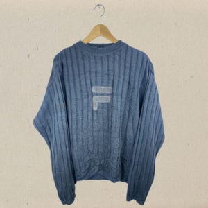 May include: A blue ribbed knit jumper with a white "F" logo on the front.