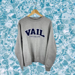 May include: Grey sweatshirt with a blue and white embroidered logo that says "Vail Colorado".