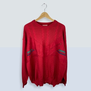 May include: Red knitted jumper with a zipped pocket and green and blue stripes on the sleeves.