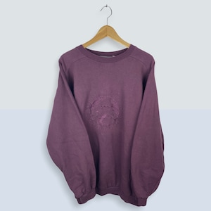 May include: A maroon sweatshirt with a large embroidered circle on the front. The circle features a globe with the text "Around the World" around it.