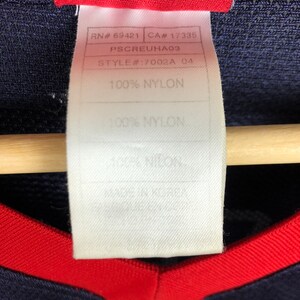 May include: A white tag with black text that reads "RN# 69421 CA# 17335 PSCREUHA03 STYLE#:7002A 04 100% NYLON 100% NYLON".