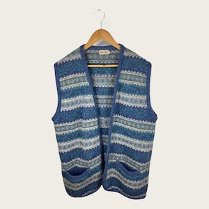 May include: A blue and white striped knitted waistcoat with two pockets. The waistcoat has a V-neck and is made of a soft, cosy material.