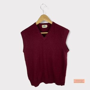 May include: A burgundy sleeveless sweater vest with a V-neck. The sweater has a small, blue and yellow label with the text "Sun Valley" on it.