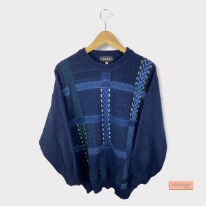 May include: A navy blue jumper with a geometric pattern in shades of blue, green, and white. The jumper has a crew neck and long sleeves. The label "NERI" is visible on the front of the jumper.