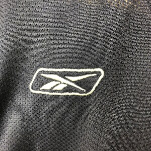 May include: Close-up of a black Reebok logo embroidered on a black fabric.