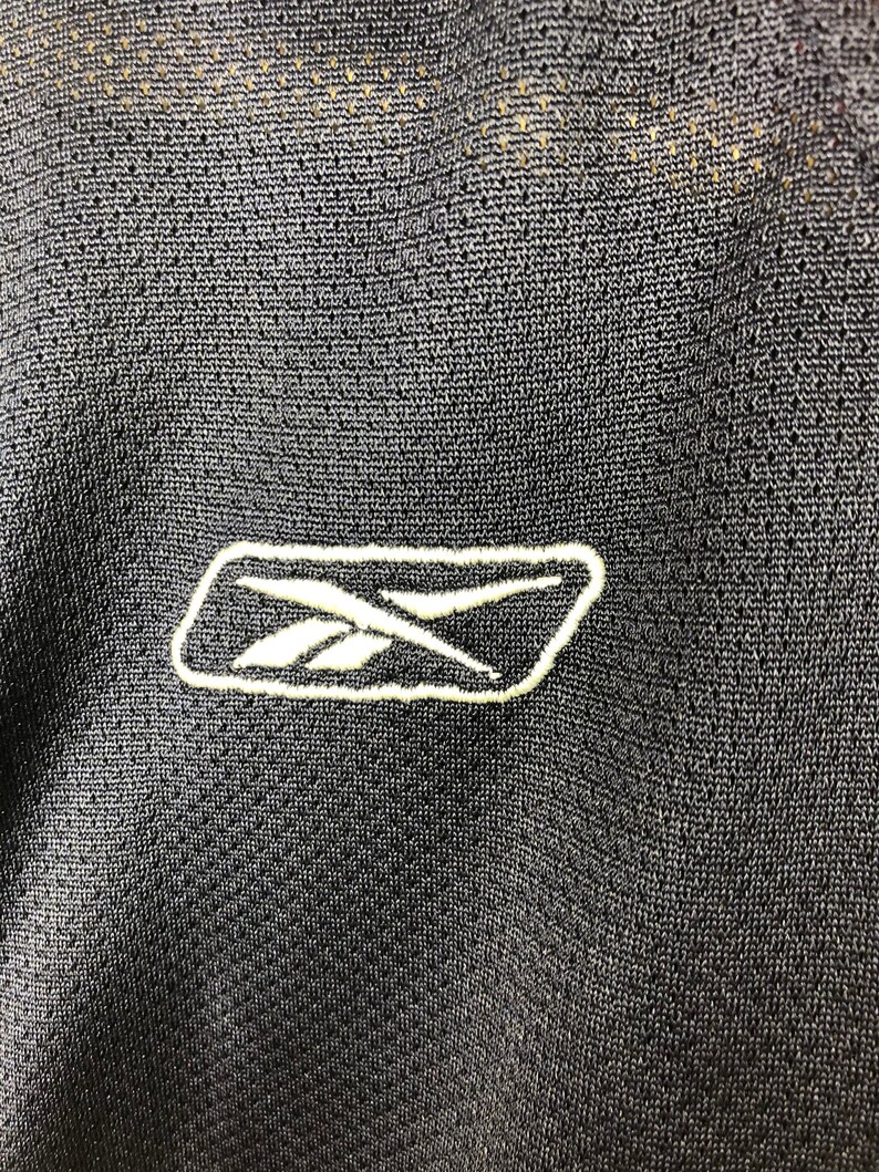 May include: Close-up of a black Reebok logo embroidered on a black fabric.