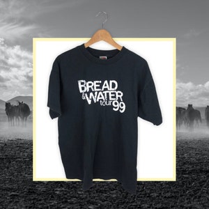 Puede incluir: Camiseta negra con un gráfico blanco que dice "Bread & Water Tour 99".