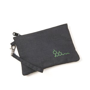 May include: A grey zipped pouch with a green chemical structure embroidered on the front. The pouch has a black zipper and a black strap with a silver clip.