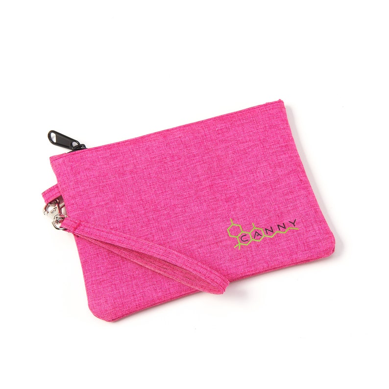 May include: A pink zippered pouch with a black zipper and a gold embroidered logo that says "CANNY".