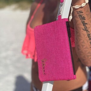 May include: A pink zippered pouch with a gold logo that says "CANNY" on it. The pouch is hanging from a black strap.