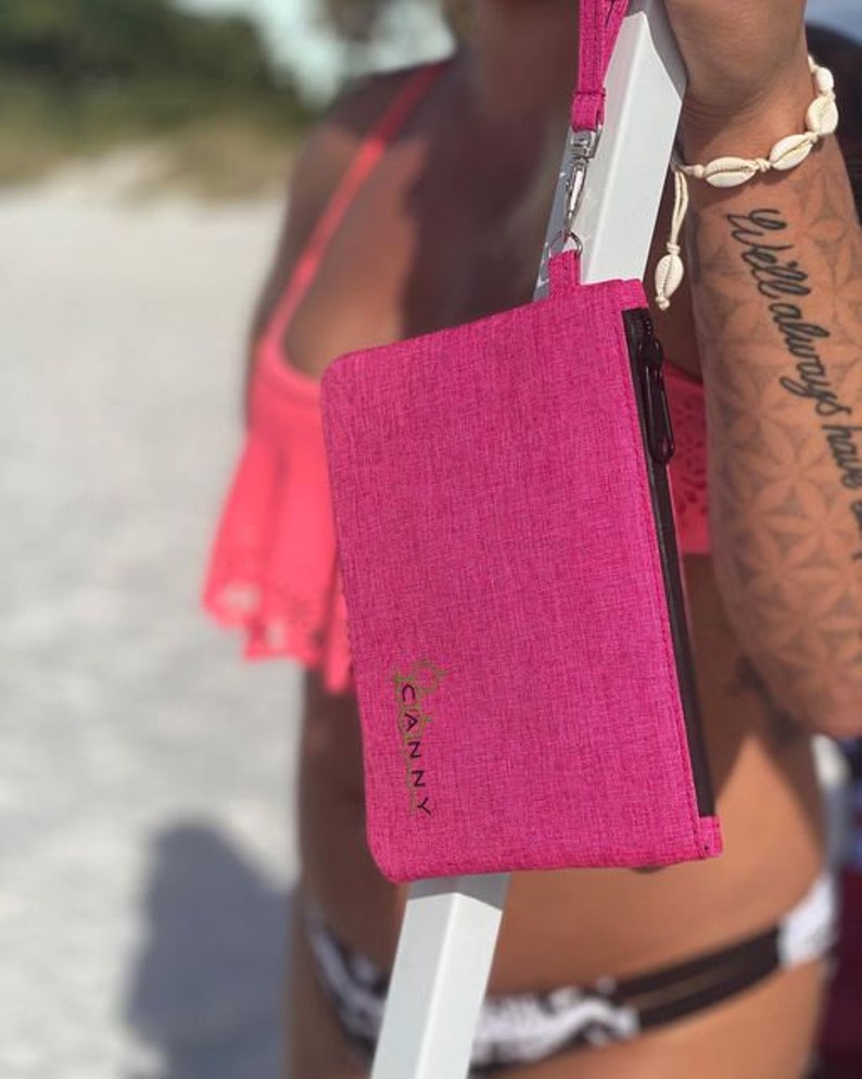 May include: A pink zippered pouch with a gold logo that says "CANNY" on it. The pouch is hanging from a black strap.
