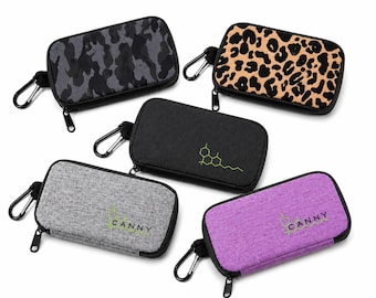 May include: Five rectangular zippered cases with carabiner clips. One features a dark gray camouflage pattern, one has a tan and black leopard print, one is solid black with a green chemical structure, one is heather gray with the text CANNY, and one is purple with the text CANNY.