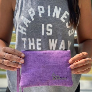 May include: A purple zippered pouch with the word "CANNY" printed in green on the front. The pouch is made of a soft, textured fabric.