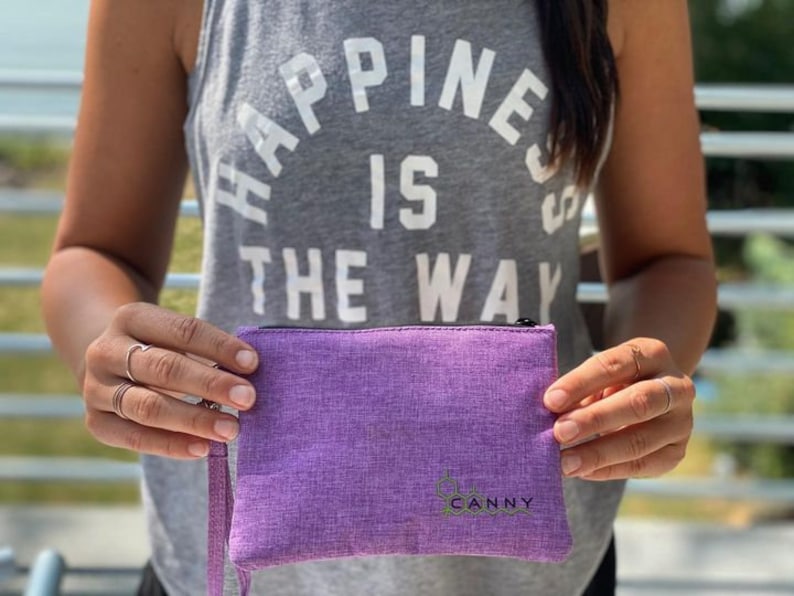 May include: A purple zippered pouch with the word "CANNY" printed in green on the front. The pouch is made of a soft, textured fabric.