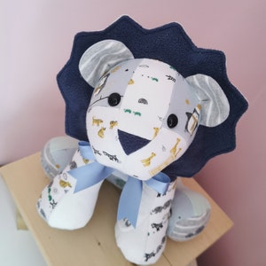 May include: A blue and white stuffed lion with a blue bow. The lion is made from fabric scraps and has a patterned design with animals and geometric shapes.