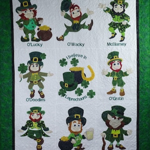 May include: A white quilt featuring appliqued leprechauns in various poses, each with a name below. The quilt has a green border and includes the text "I believe in Leprechauns" with shamrocks, a horseshoe, and a pot of gold.