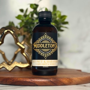 Puede incluir: Una botella de vidrio de jarabe de margarita de coco y habanero Middleton's. La botella es de 240 ml y tiene una etiqueta negra con letras doradas. La etiqueta dice "Artisan Cocktail Bitters & Supplies".