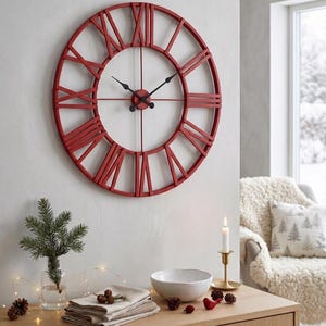 May include: A large, circular wall clock featuring a red metal frame with open-work Roman numerals. The clock has thin black metal hands at the centre. The design is minimalist, consisting of a circular outer ring and radial spokes connecting to the centre.