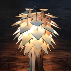 Peut inclure: Lampe de table en bois au design unique. L'abat-jour est compos&eacute; de pi&egrave;ces de bois en forme de losange. Le pied pr&eacute;sente une conception ouverte et artistique. La lampe est allum&eacute;e, d&eacute;gageant une lueur chaleureuse.