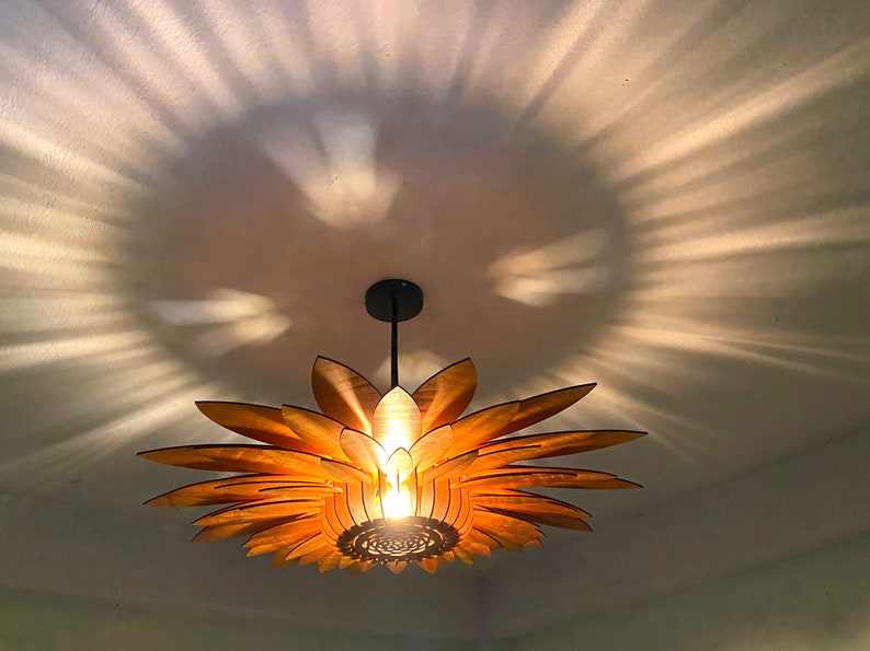 Puede incluir: Una l&aacute;mpara colgante de madera con forma de girasol con una bombilla c&aacute;lida que ilumina la habitaci&oacute;n. La l&aacute;mpara proyecta un patr&oacute;n de luz y sombra en el techo.
