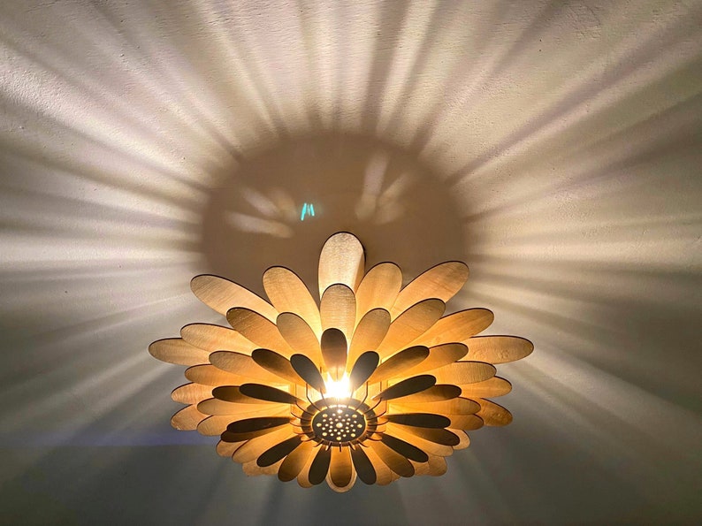 May include: A wooden ceiling light fixture shaped like a flower with multiple layers of petals. The light is on and casts a warm glow.