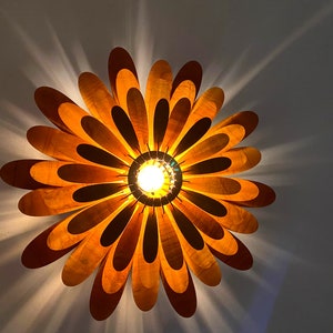 May include: A wooden ceiling light fixture shaped like a flower with a warm yellow light shining through the centre.