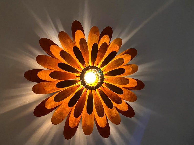 May include: A wooden ceiling light fixture shaped like a flower with a warm yellow light shining through the centre.