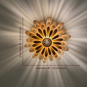 May include: A wooden ceiling light fixture shaped like a flower with 26.8 inch diameter. The light fixture has a warm, golden hue and is made of multiple layers of wood.