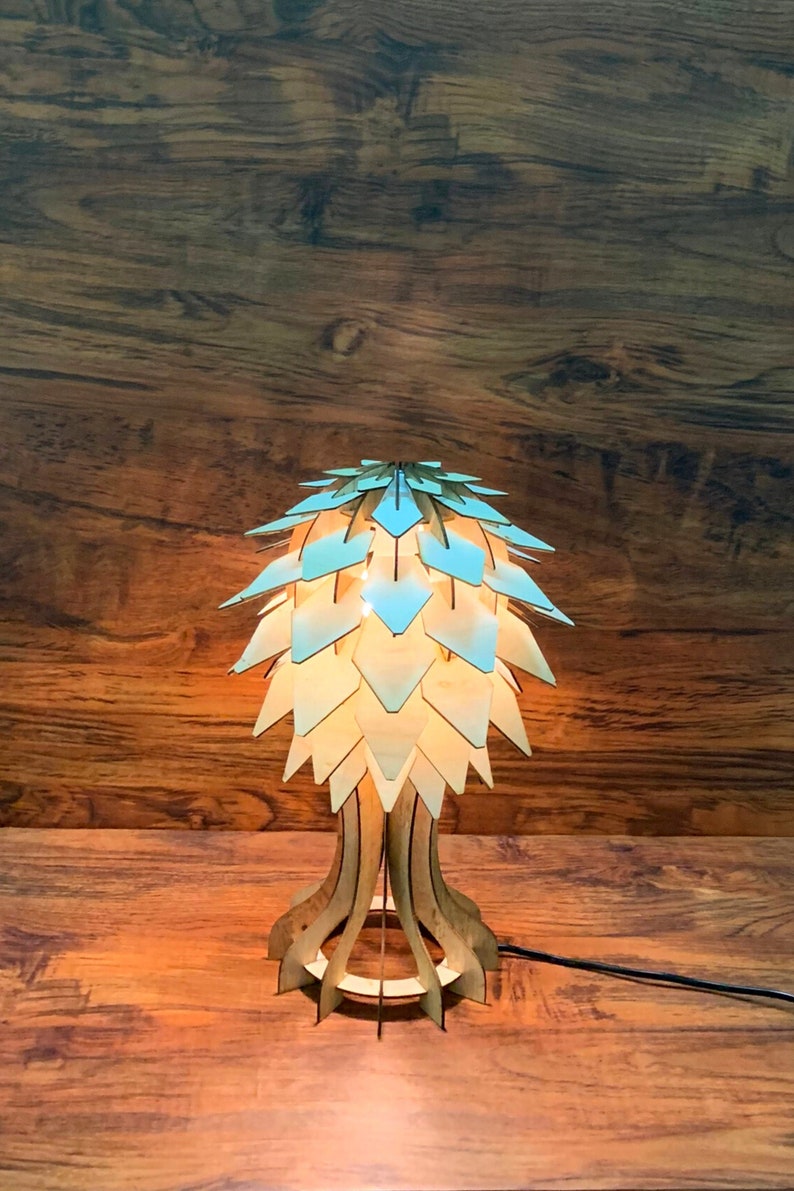 Op de afbeelding: Een houten tafellamp met een lichtblauwe en witte geometrische lampenkap. De lamp staat op een houten oppervlak.