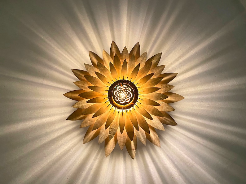 Op de afbeelding: Een gouden metalen plafondlamp in de vorm van een zonnebloem met een centrale gloeilamp.