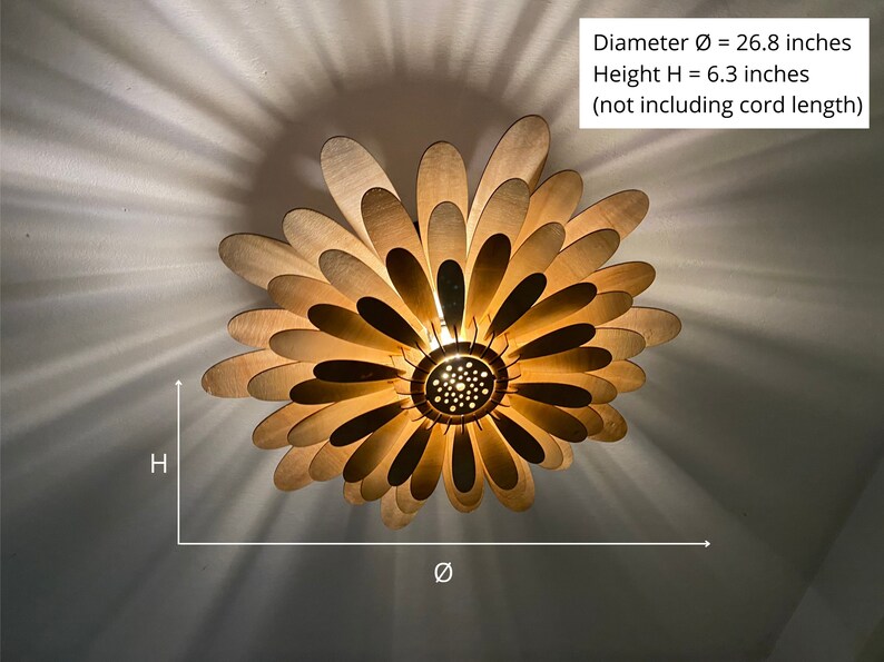 May include: A wooden ceiling light fixture shaped like a flower with 26.8 inches in diameter and 6.3 inches in height. The light fixture has a warm, golden glow and is made of many thin, wooden petals.
