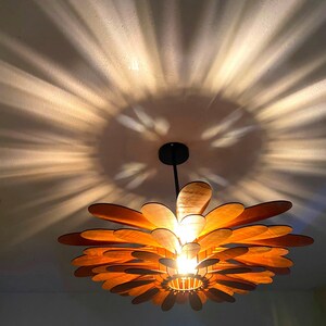 May include: A wooden ceiling light fixture shaped like a flower with multiple layers of petals. The light fixture is hanging from the ceiling and casting a shadow on the wall.