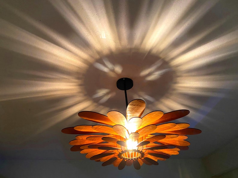 May include: A wooden ceiling light fixture shaped like a flower with multiple layers of petals. The light fixture is hanging from the ceiling and casting a shadow on the wall.
