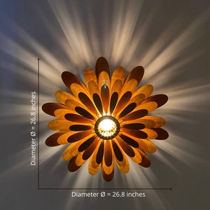 May include: A wooden ceiling light fixture shaped like a flower with a 26.8 inch diameter. The light fixture has a warm, golden brown colour and is made of many thin, overlapping wooden petals.