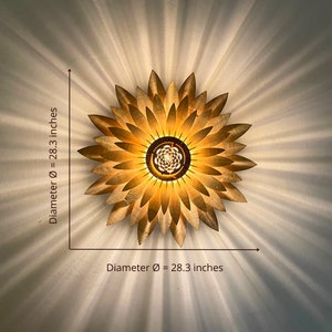 Op de afbeelding: Een gouden metalen plafondlamp in de vorm van een zonnebloem met een diameter van 72 cm. De lamp heeft een cirkelvormig midden met meerdere lampen.