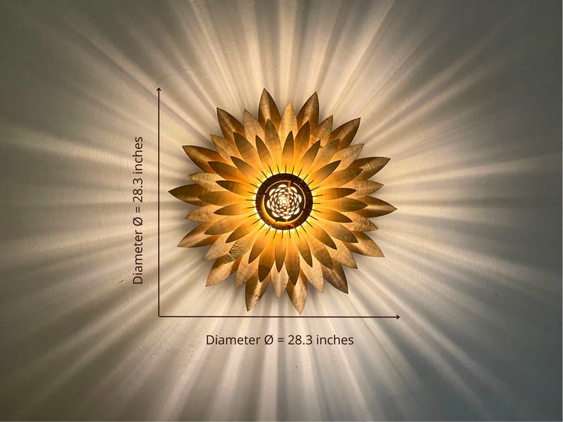 Op de afbeelding: Een gouden metalen plafondlamp in de vorm van een zonnebloem met een diameter van 72 cm. De lamp heeft een cirkelvormig midden met meerdere lampen.
