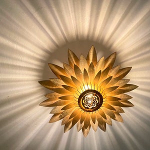 Op de afbeelding: Een gouden plafondlamp in de vorm van een zonnebloem met een centrale gloeilamp.