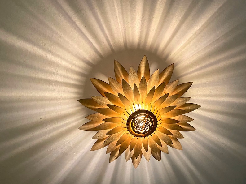 Op de afbeelding: Een gouden plafondlamp in de vorm van een zonnebloem met een centrale gloeilamp.