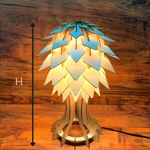 Peut inclure: Lampe de table en bois au design unique, avec un abat-jour en forme de feuilles superpos&eacute;es dans des tons de bleu clair et de bois naturel. La lampe mesure 42 cm de haut et 19 cm de diam&egrave;tre. La lampe est allum&eacute;e, d&eacute;gageant une lueur chaleureuse.