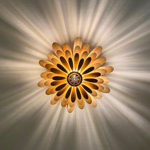 May include: A gold-colored ceiling light fixture shaped like a flower with multiple petals. The light is on and casting a warm glow.