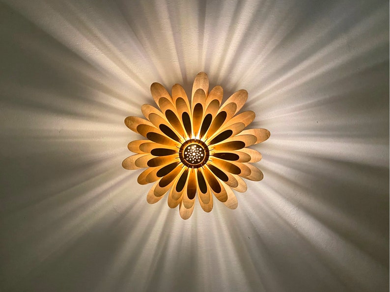May include: A gold-colored ceiling light fixture shaped like a flower with multiple petals. The light is on and casting a warm glow.