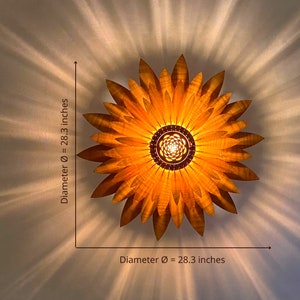 Puede incluir: Una l&aacute;mpara de madera con forma de girasol de 72 cm de di&aacute;metro. La l&aacute;mpara tiene un tono dorado c&aacute;lido y se ilumina desde el centro.